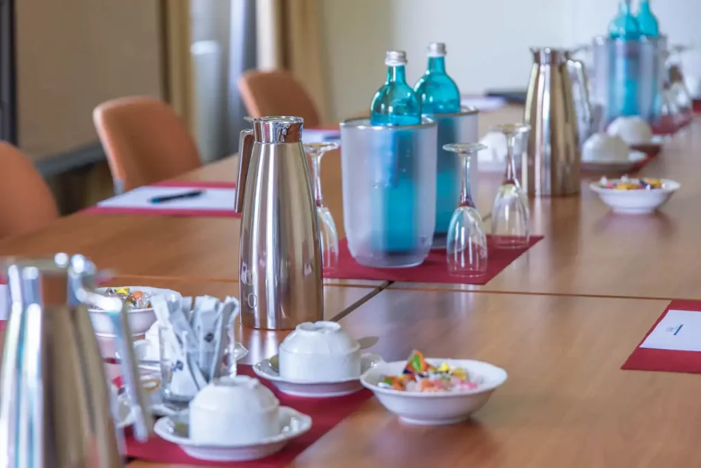 Close up eines Tischs im Tagungsraum des Eurohofs mit Kaffeekannen, Kaffeetassen, Wasserflaschen in Kühlern und Gummibärchen